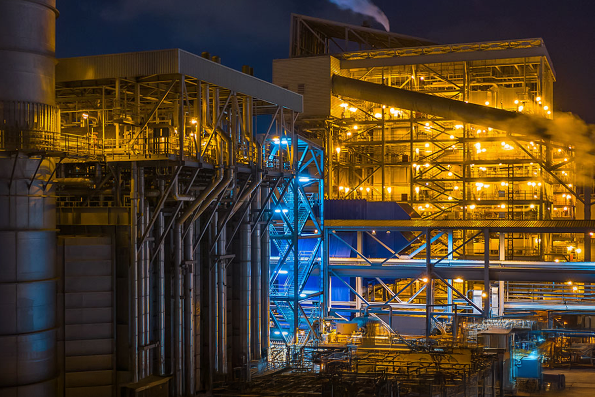 Visão noturna de uma grande instalação industrial com estruturas iluminadas, armações metálicas e canos interconectados brilhando, ilustrando artigo sobre o que são lúmens