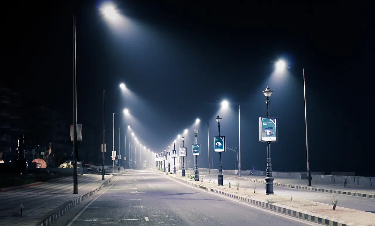 Imagem de uma rua vazia durante a noite, com postes de iluminação LED distribuídos ao longo da via, iluminando toda a rua de maneira uniforme.