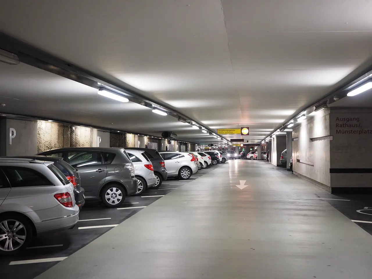 Imagem de um estacionamento interno bem iluminado, com vários carros estacionados.