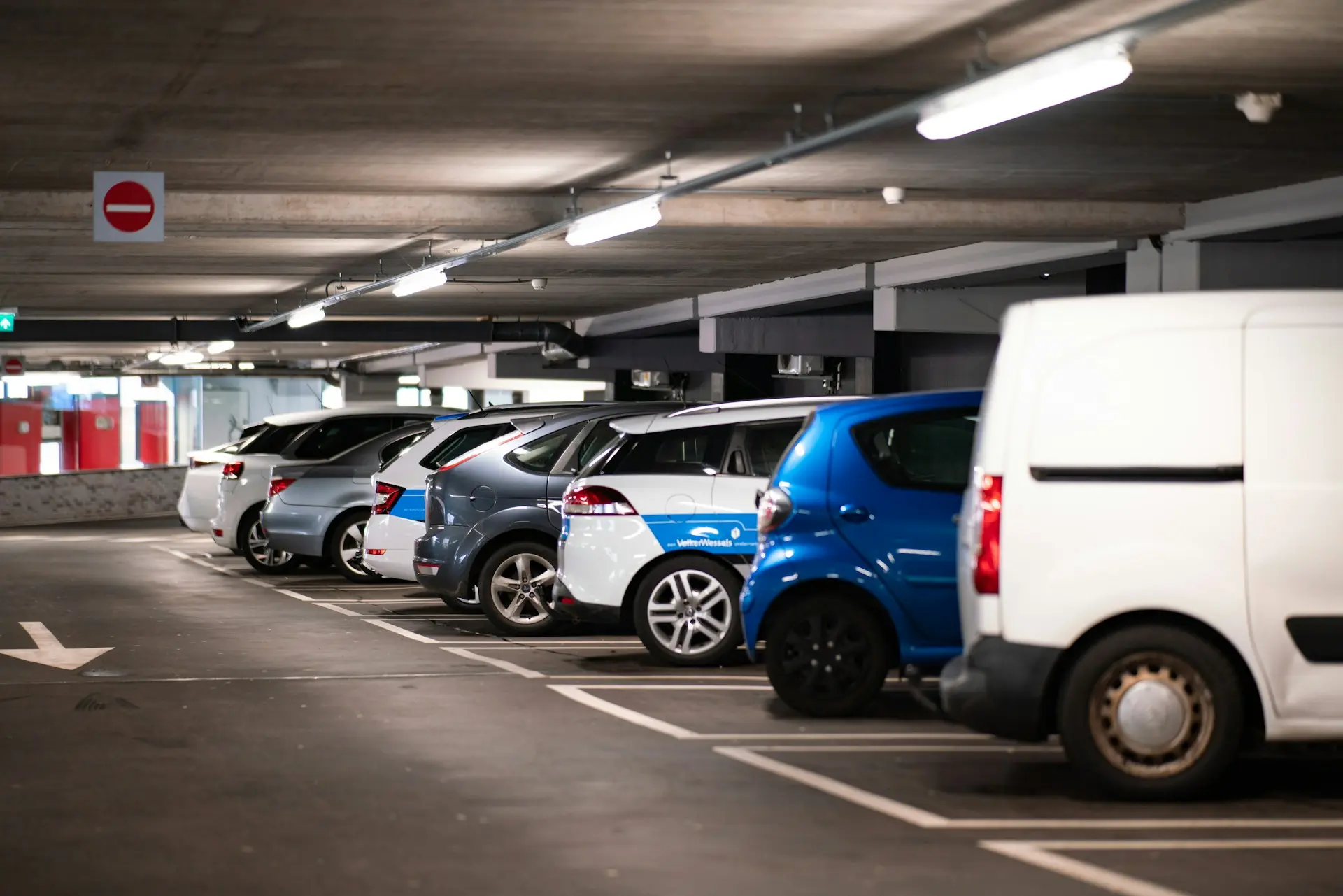 Imagem de um estacionamento interno bem iluminado, com vários carros estacionados.