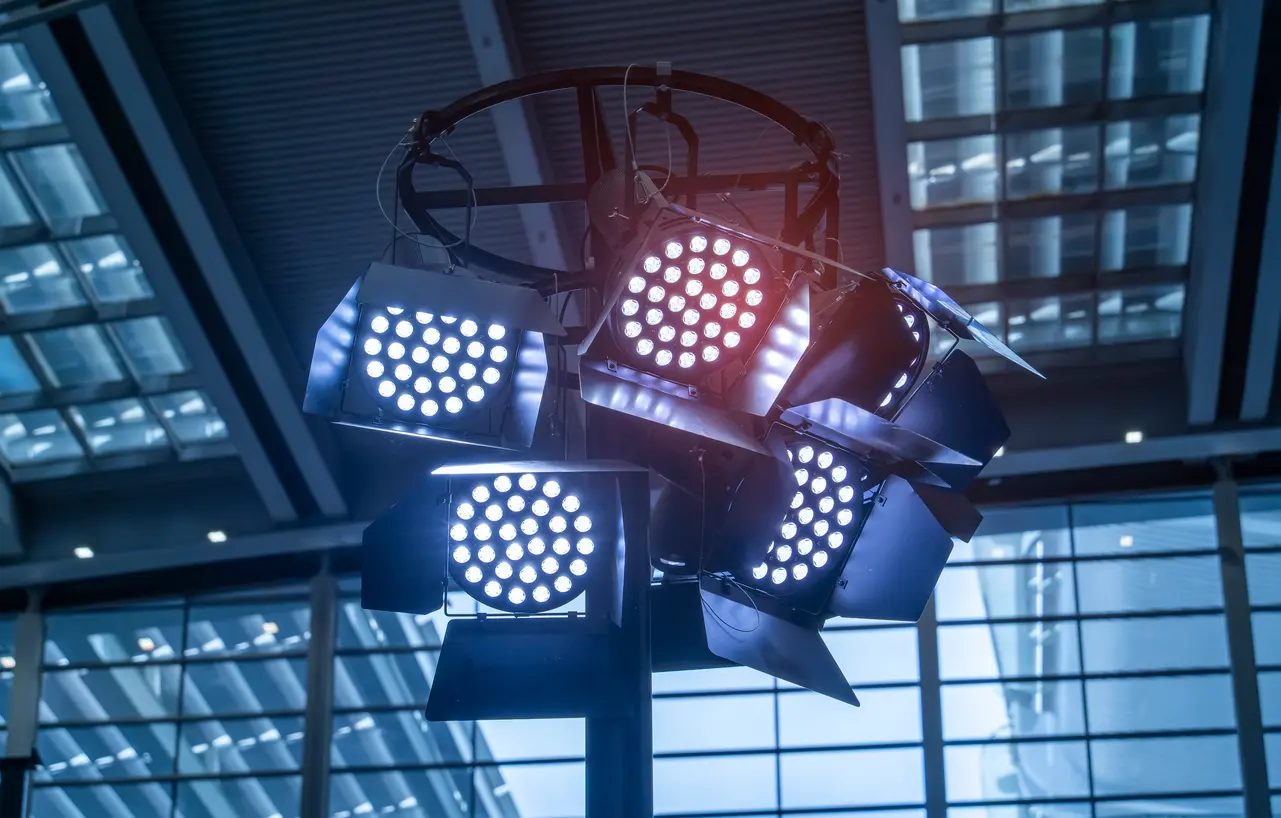 Refletores LED profissionais agrupados em uma estrutura circular, instalados em um ambiente interno amplo. As luzes variam entre tons frios e quentes, indicando a importância do IRC na fidelidade das cores.