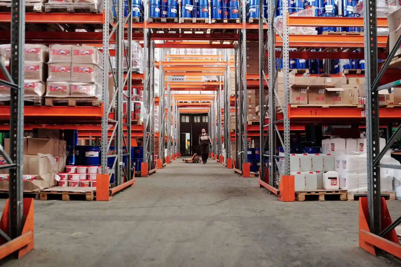 Imagem mostra um corredor de um centro de distribuição com diversas caixas empilhadas ao longo das prateleiras.