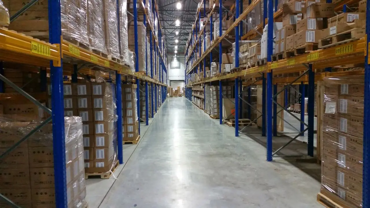 Imagem mostra um corredor de um centro de distribuição com diversas caixas empilhadas ao longo das prateleiras.