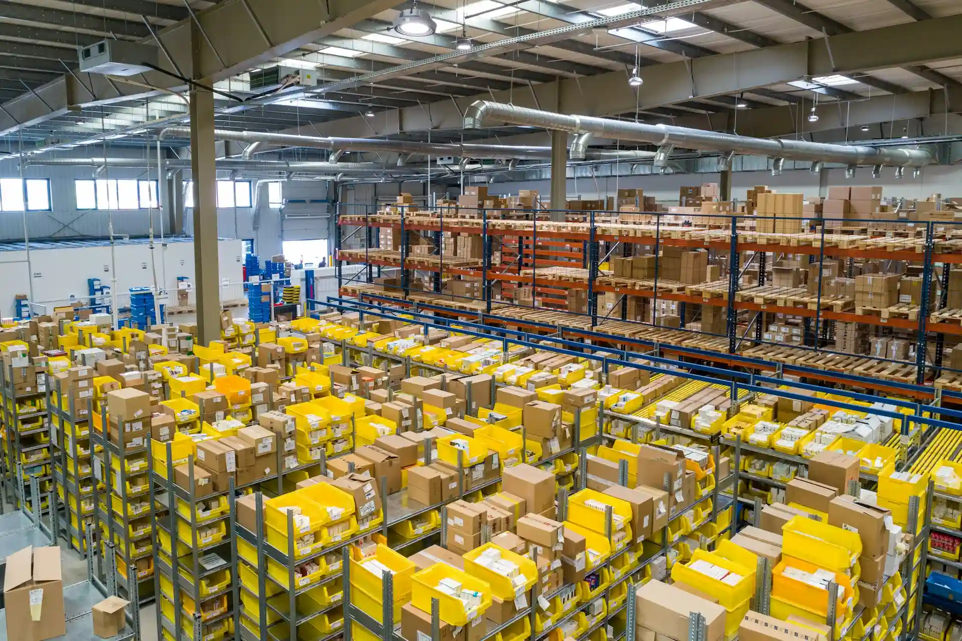 iluminacao-docas-de-carga-e-descarga Imagem de um galpão com diversas mercadorias armazenadas em pallets e prateleiras.
